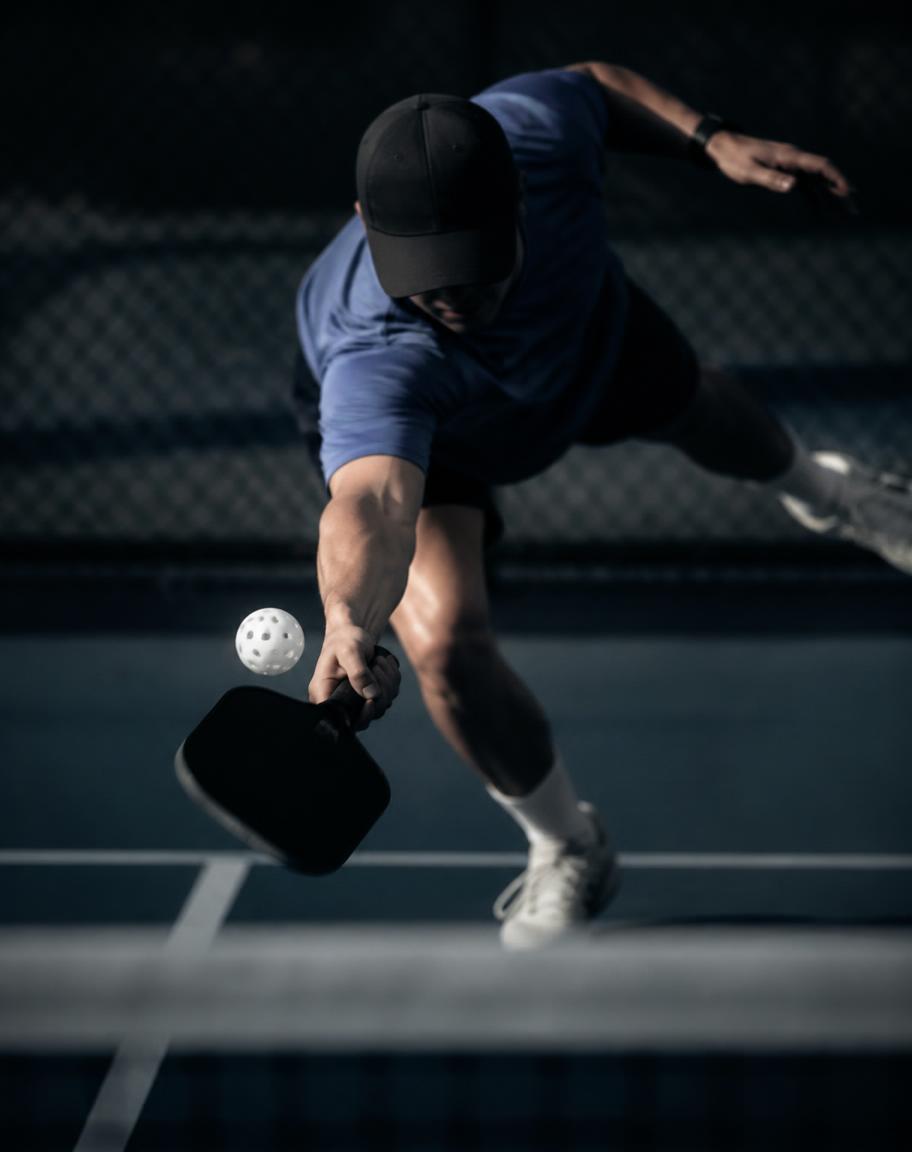Athlete diving low for a pickleball volley on a floodlit court